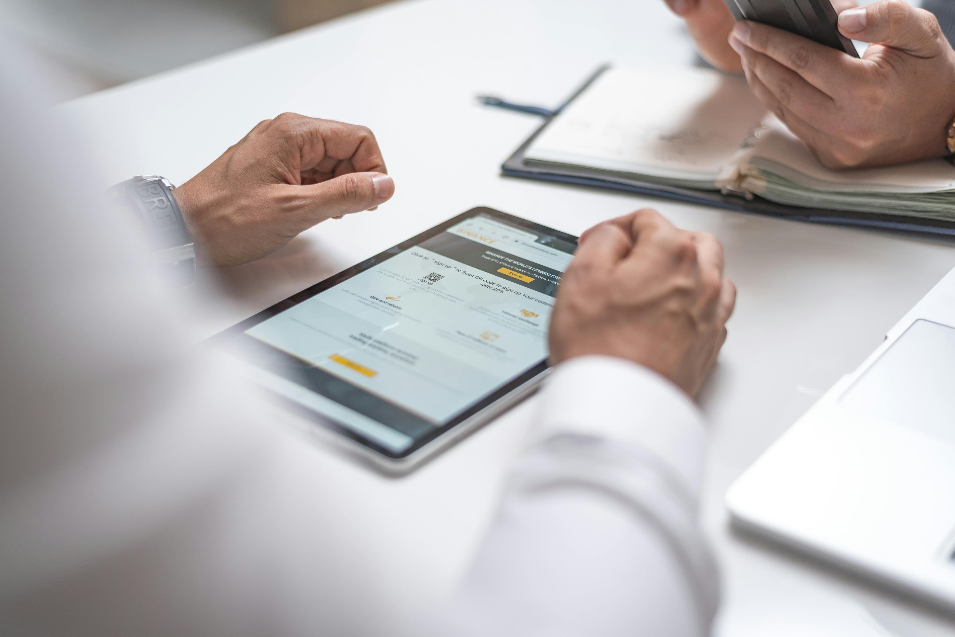 Team members collaborating at a desk with a tablet and notebook